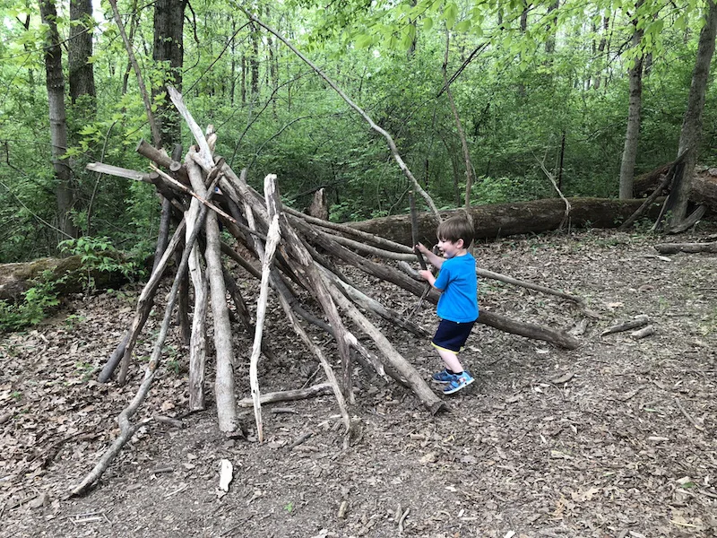 boy playing in a stick fort at the Natural Play Area