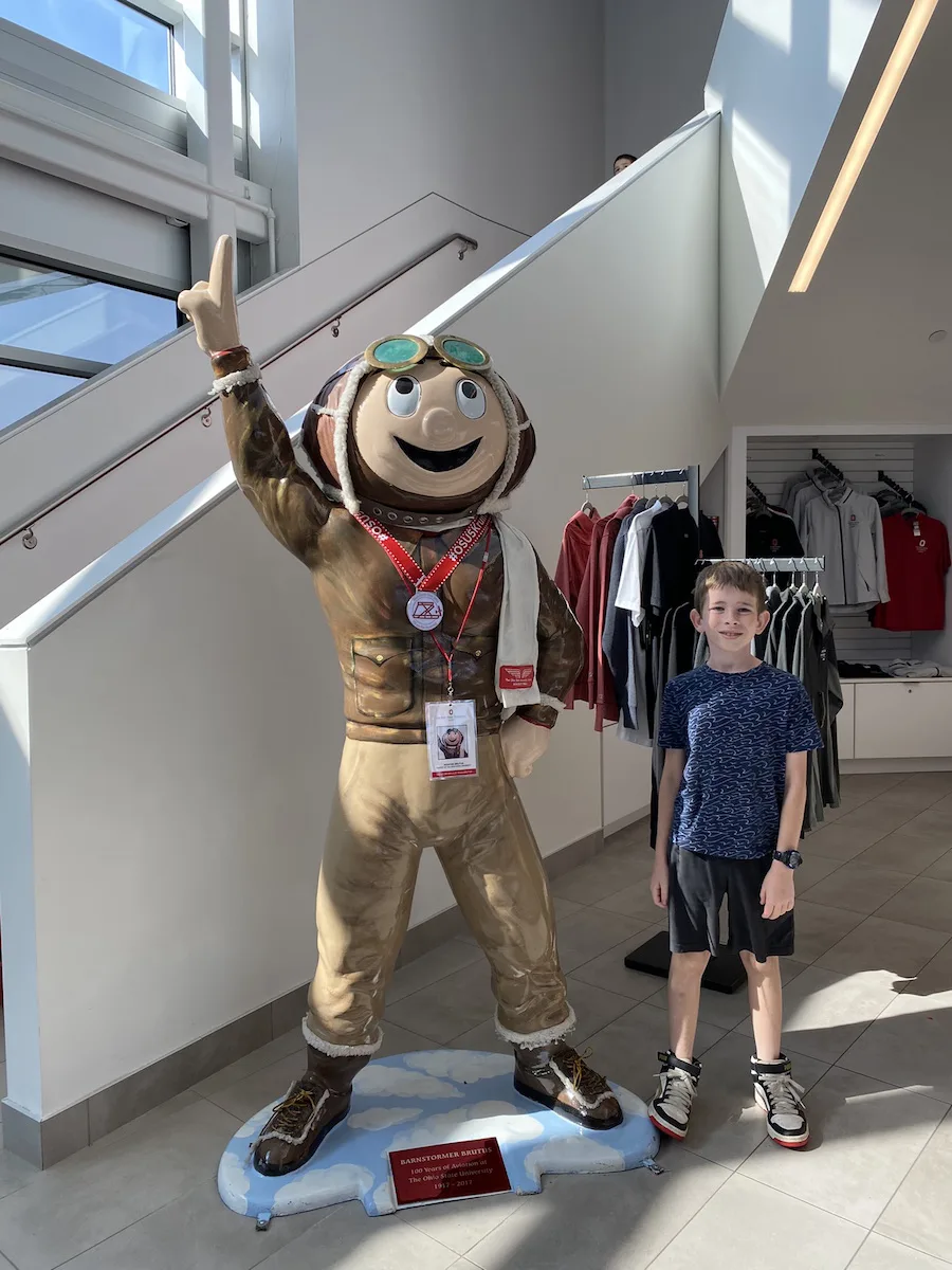 boy standing next to Brutus Buckeye at the Ohio State University Airport.