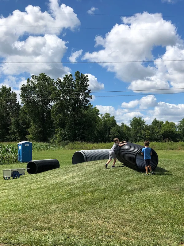 two boys pushing an empty tube up a hill to roll down at Hendren Farm Market