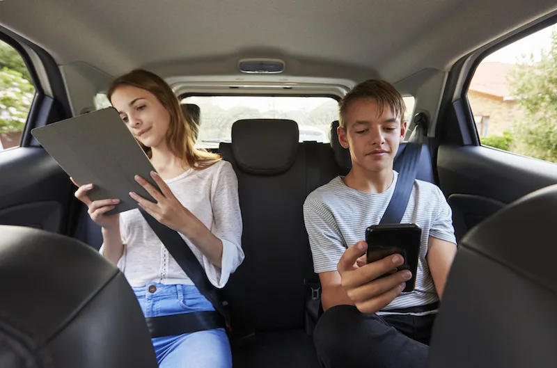 boy and girl looking at devices in the car