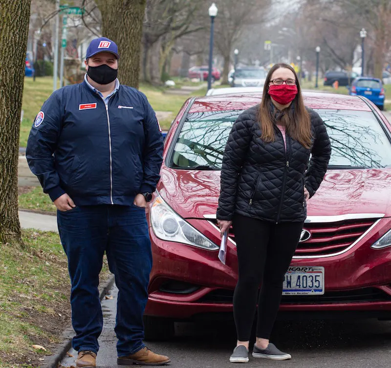 man and woman standing in front of a red car.