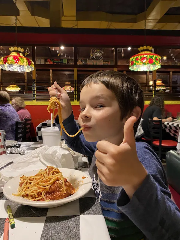boy eating spaghetti and giving a thumbs up.