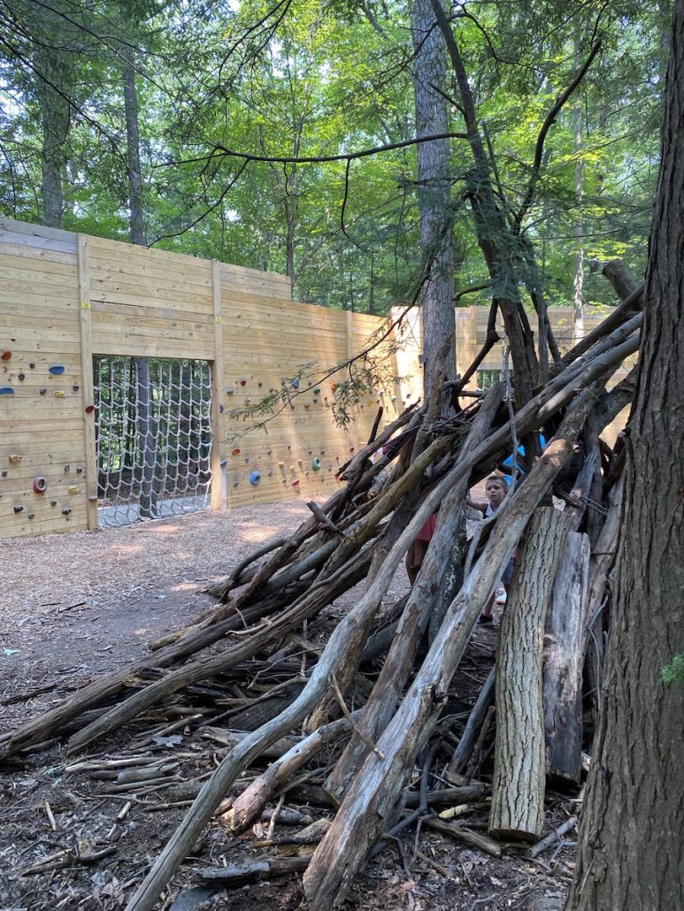 Fort made of sticks in the foreground and rock climbing wall in the background at Jordan Creek Park.