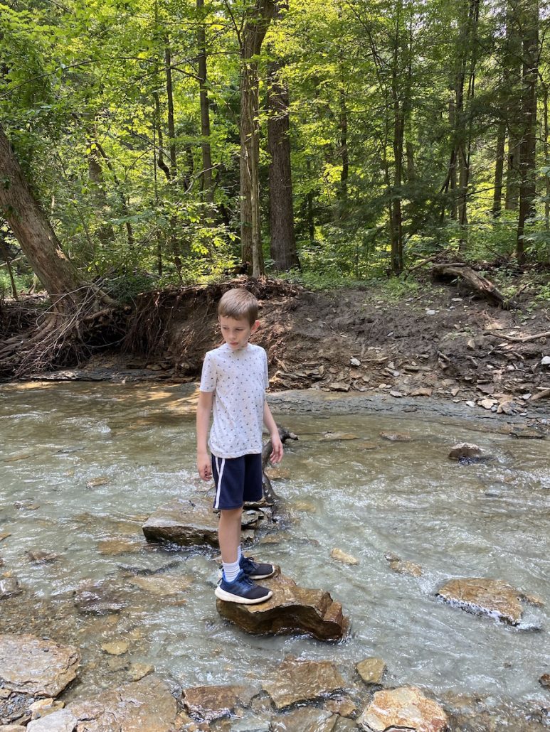 Boy standing on a rock in the middle of Jordan Creek.