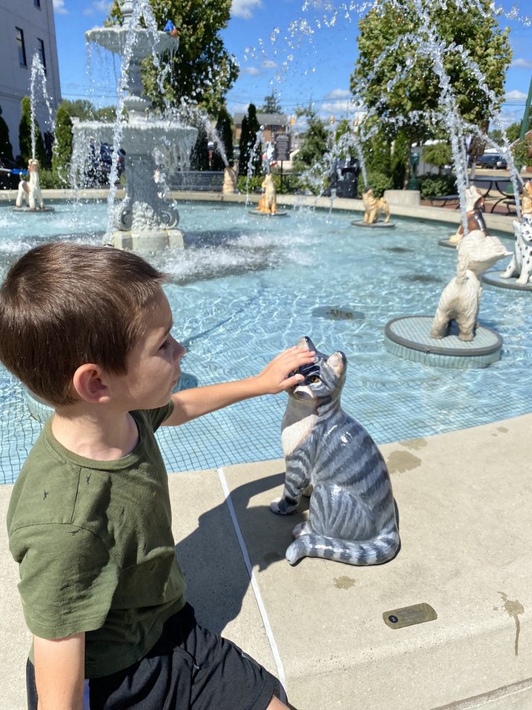A boy petting a cat statue at the Dog Fountain in Mount Vernon, Ohio.