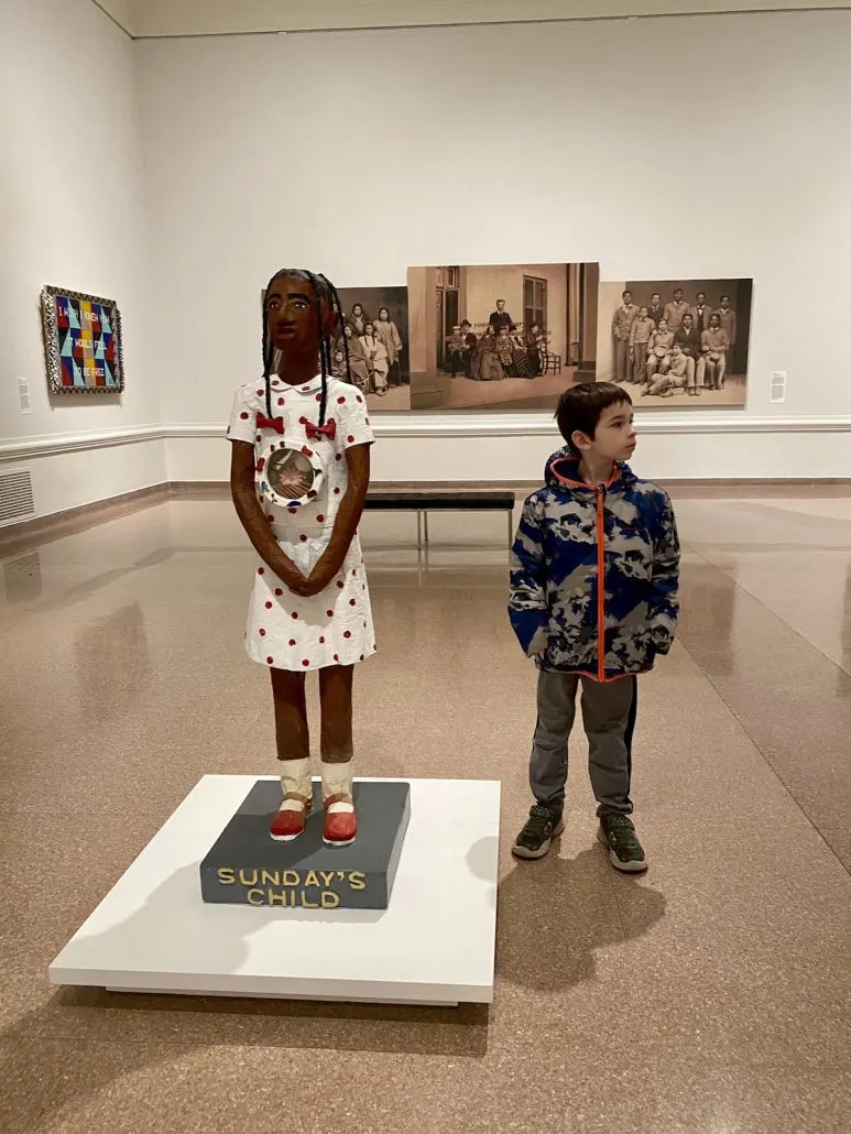 A boy standing next to a statue of a girl in the Speed Art Museum in Louisville, Kentucky.