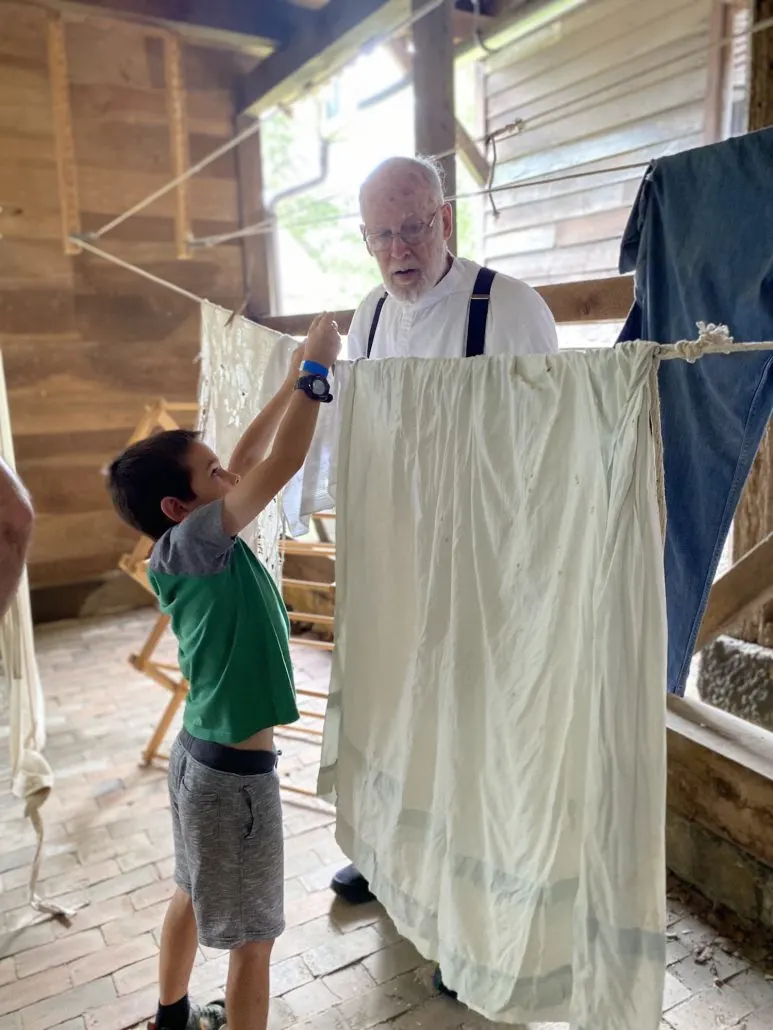 A boy learning to hang up laundry with a re-enactor at Zoar Village, a historical town in Ohio.