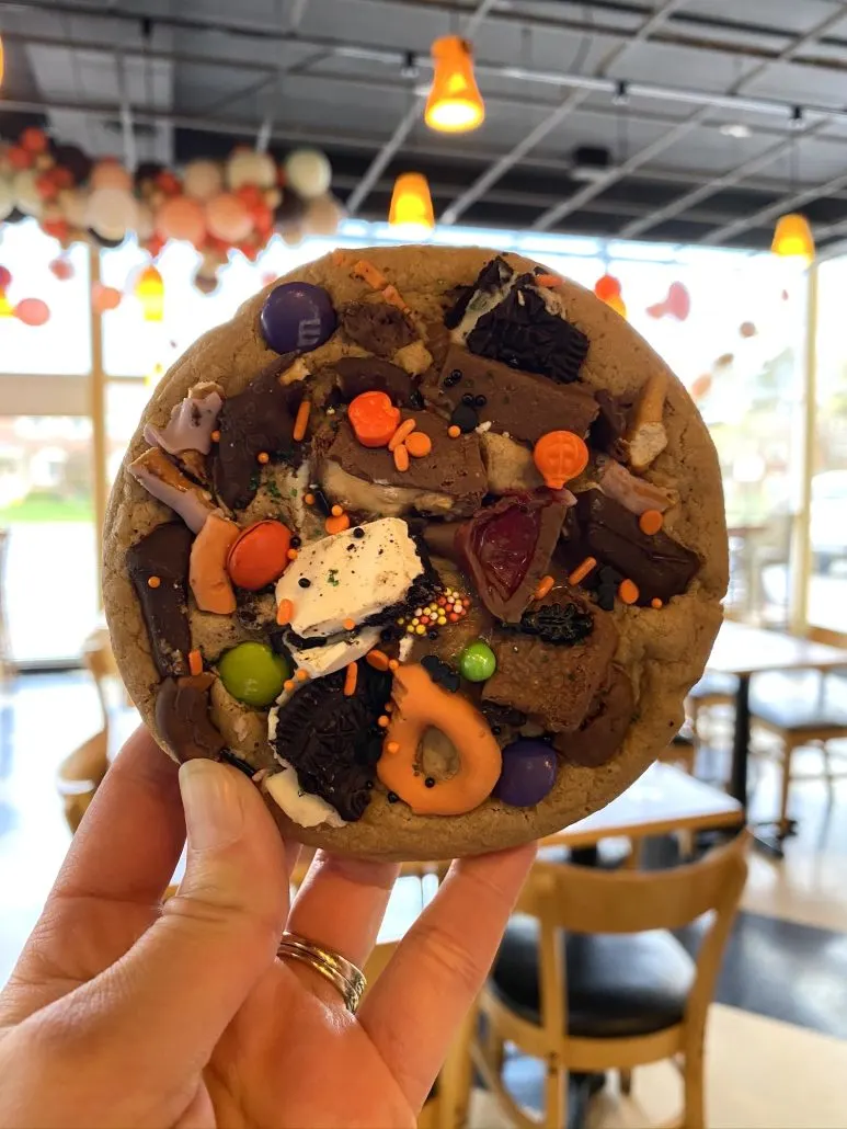 A chocolate chip cookie with lots of toppings held up in front of the window at Chocolate Cafe, a restaurant near Grandview Ohio.