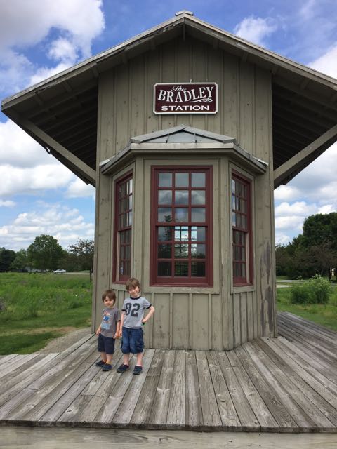 Two boys standing in front of a train depot replica called Bradley Station in Homestead Metro Park.