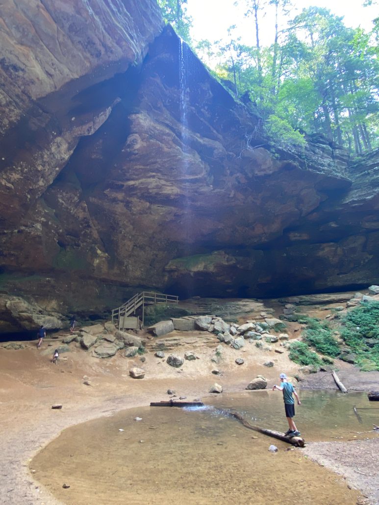 Boy standing on a log in a pool of water under the waterfall at Ash Cave in Ohio.