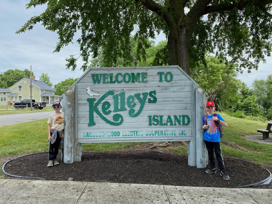Two boys standing in front of the "Welcome to Kelleys Island" sign.