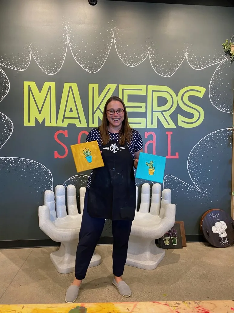 A woman holding up two craft projects done at Makers Social in Columbus, Ohio.