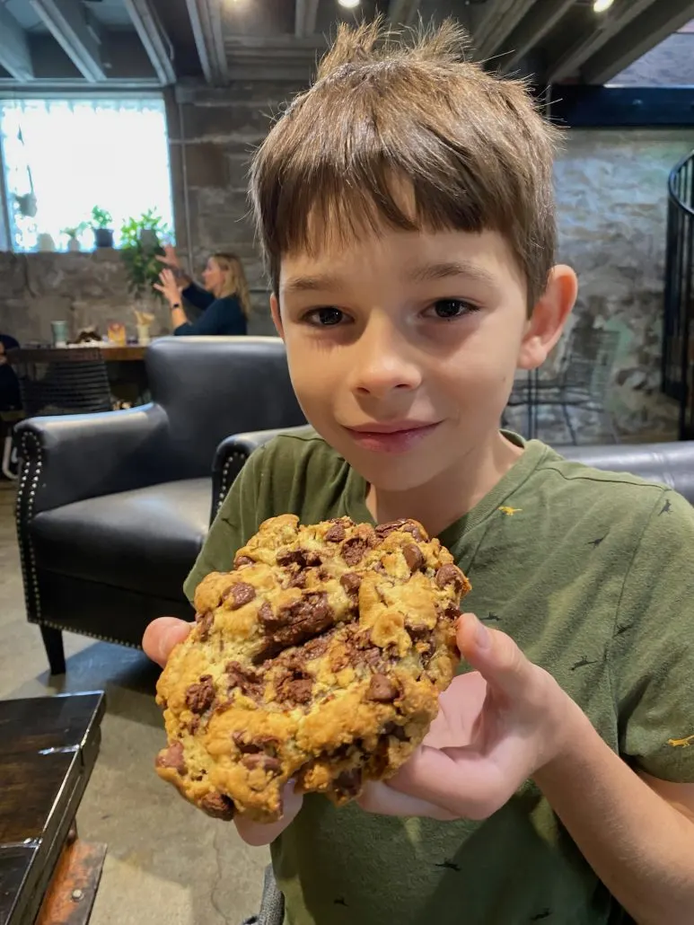 A boy holding up a chocolate chip cookie.
