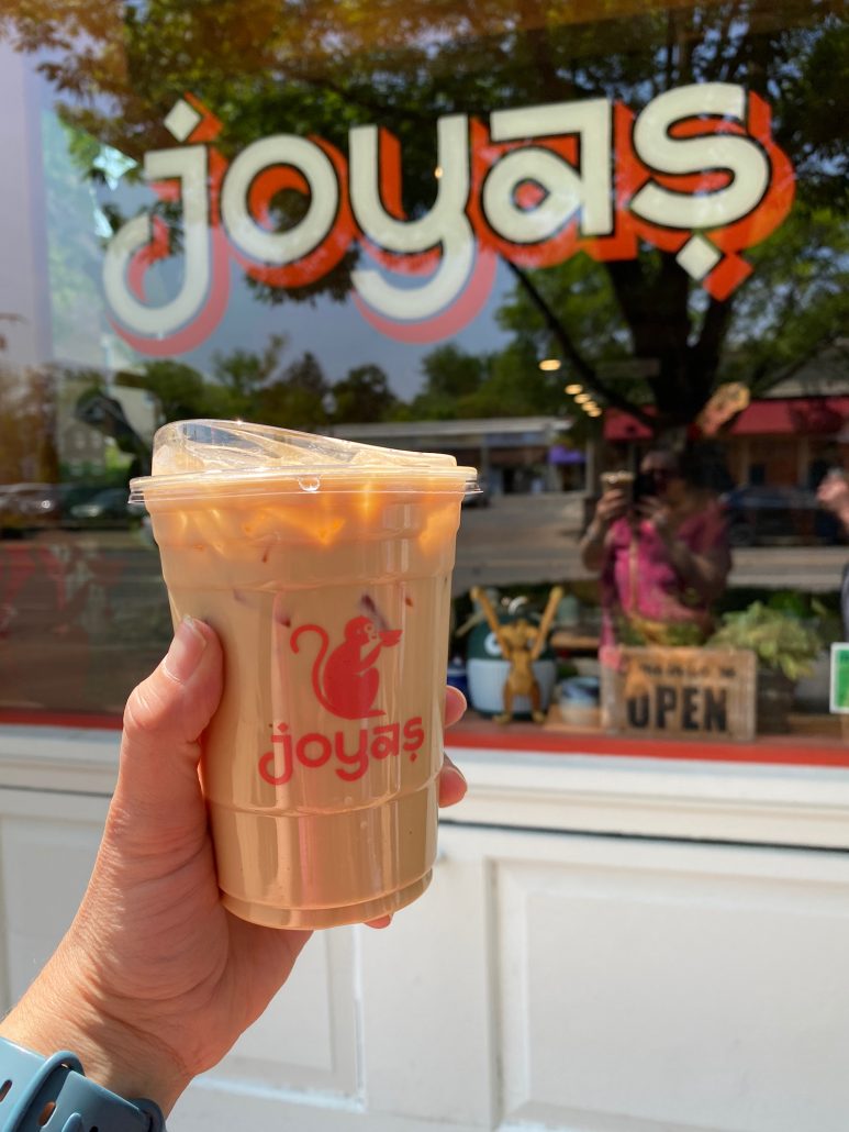 A hand holding up a Joya's Latte outside the restaurant. 