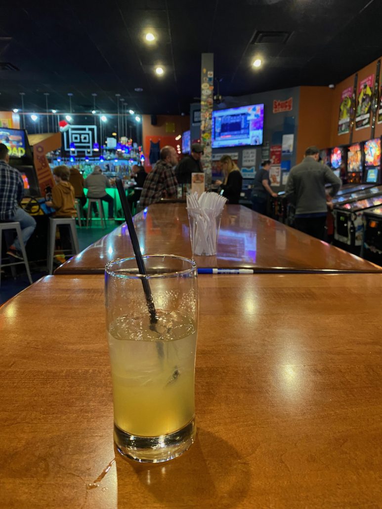 A drink on a table in front of arcade games and pin ball games at Level One Arcade and Bar.