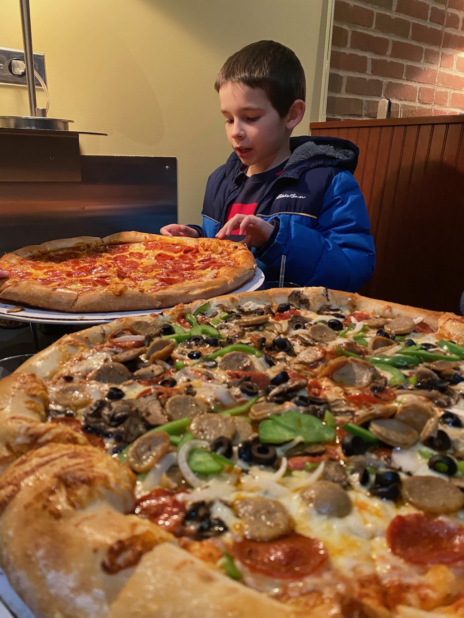 Two large pizzas and a boy taking a piece inside Dewey's Pizza restaurant.  