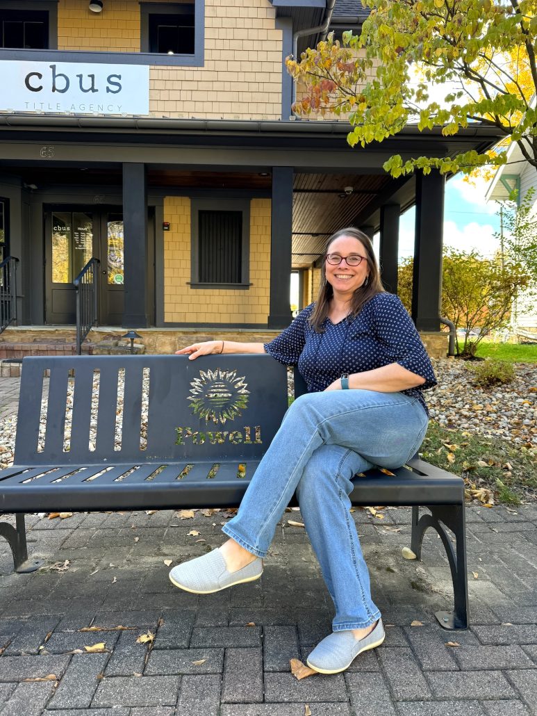 A woman sitting on a bench that says Powell.