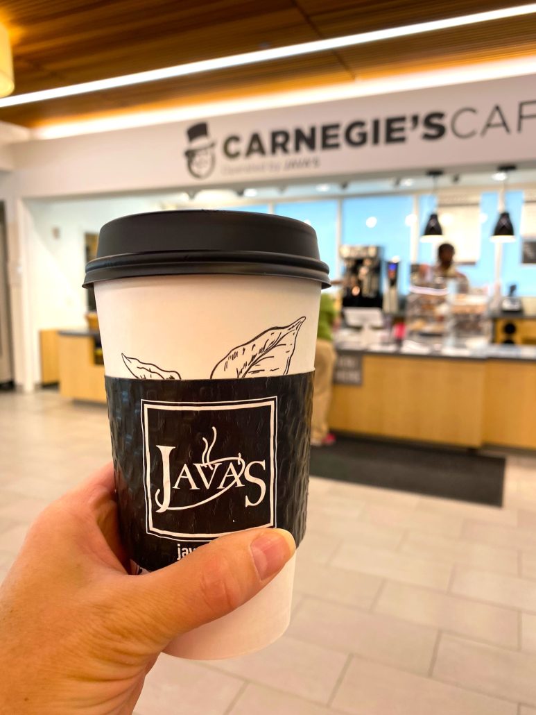 A cup of coffee held up in front of Carnegie's Cafe at Main Library in Columbus, Ohio.