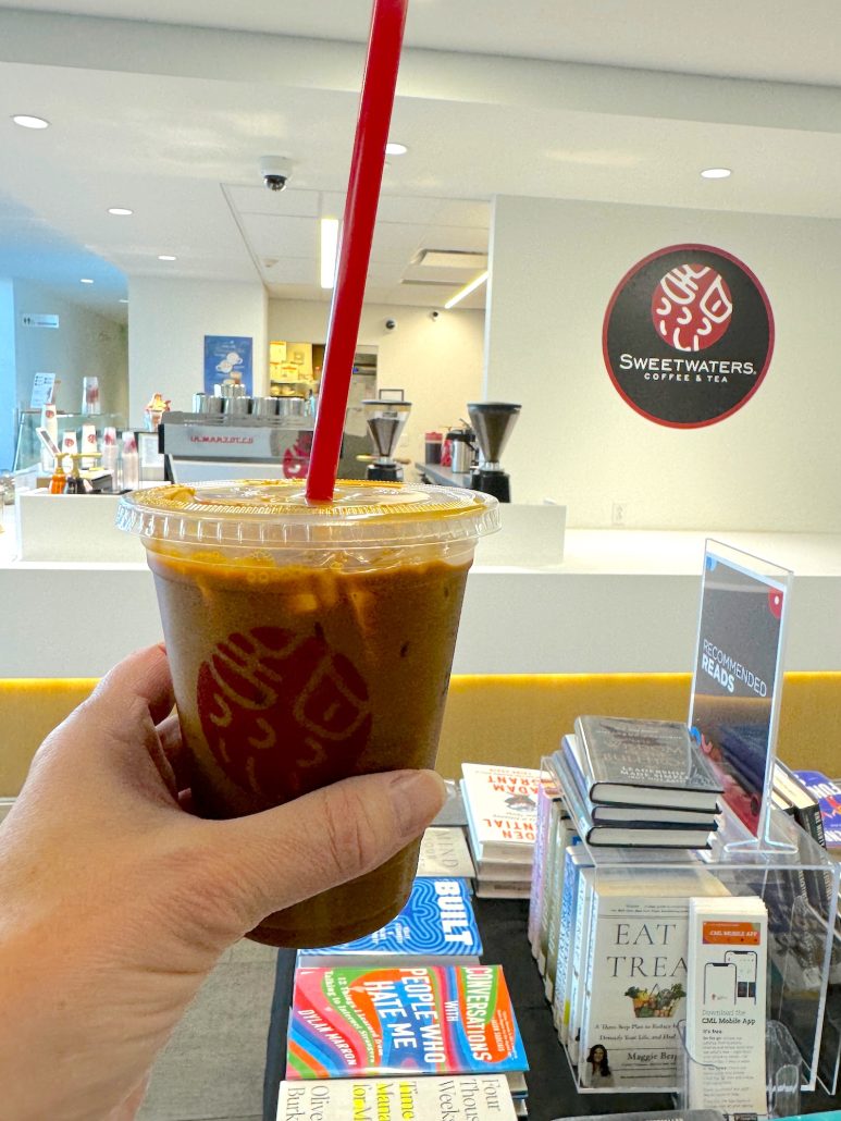 An iced coffee with straw held up in front of the coffee shop inside the Dublin Library.