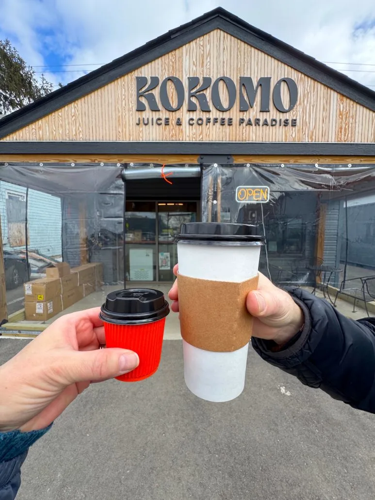 Two cups of coffee held up in front of the outside of Kokomo Coffee & Juice on the South Side of Columbus.